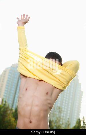 Young Athletic Man Pulling Off Shirt in Park Stock Photo