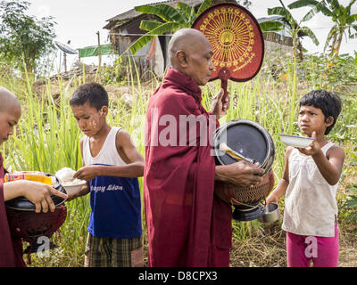 May 25, 2013 - Mae Sot, Tak, Thailand - Burmese children wait to give food to a group of Burmese monks and novices in an unofficial village of Burmese refugees north of Mae Sot, Thailand. Their community is about 50 metres from the Burmese border with Thailand. About 200 people live in thatched huts spread throughout the community. They're close enough to Mae Sot that some can work in town and Burmese merchants from Mae Sot come out to their village to do business with them. The Burmese in the village don't residency papers for Thailand and are technically considered illegal immigrants. Fifty  Stock Photo