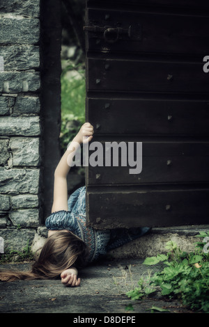 a young girl lying on the ground near an old door, trying to get up