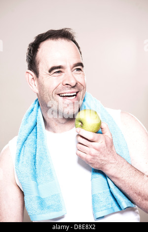 Laughing man with towel around neck holding an apple, portrait Stock Photo
