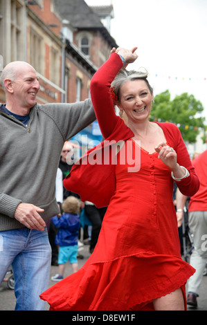 Happy laughing woman wearing a red dress dancing in the streets, UK. Couple dancing together. Stock Photo