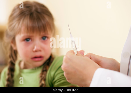 Doctor in his practice with syringe and a little girl child, she is very concerned and fearful of the treatment Stock Photo