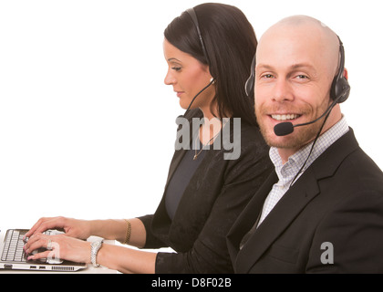 Happy businessman looking at camera and focused businesswoman typing on a laptop computer with headsets Stock Photo