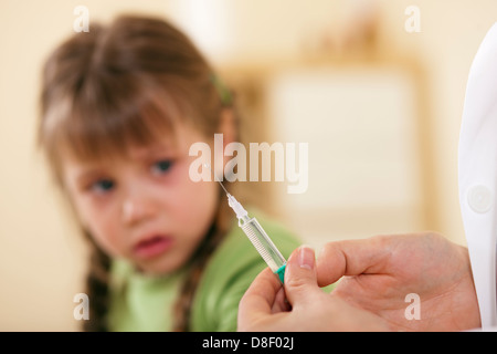 Doctor in his practice with syringe and a little girl child, she is very concerned and fearful of the treatment Stock Photo