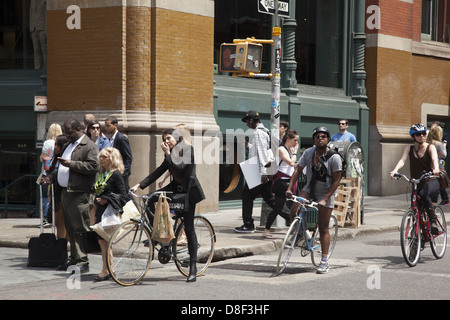Pedestrians and bicyclists wait to cross Broadway along Prince St. in the SOHO neighborhood of Manhattan Stock Photo