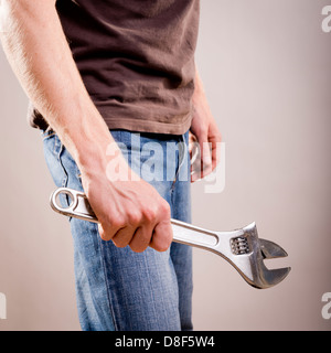 A young man dressed in casual clothes holds a large adjustable wrench or spanner Stock Photo