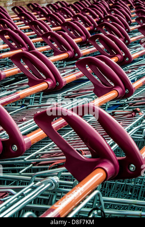 Closeup of the orange and red handles of rows of neatly parked supermarket shopping trolleys outside a UK Sainsbury's supermarket. Stock Photo