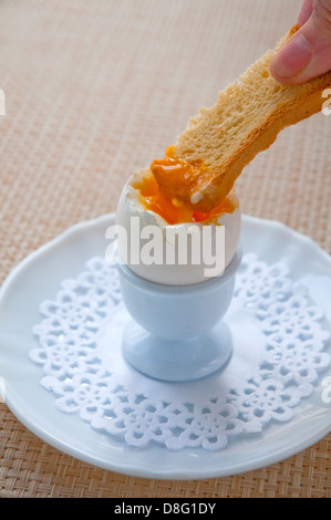 Hand dipping a piece of bread in a boiled egg. Close view. Stock Photo