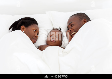 happy african american couple talking on bed with baby boy in middle sleeping Stock Photo