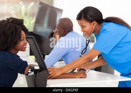 happy African medical nurse measuring patient's blood pressure in doctor's office Stock Photo