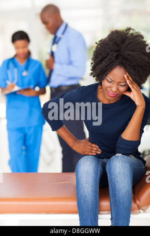 African ill woman sitting in doctors room with doctor and nurse on background Stock Photo
