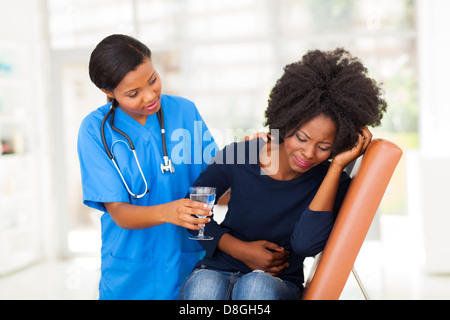 caring young African American nurse offering sick patient water Stock Photo