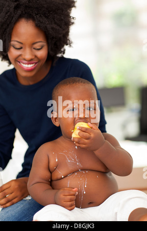 funny African baby boy eating an apple with milk spilt all over his body Stock Photo