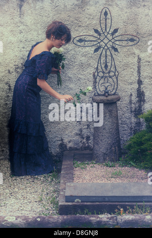 a grieving woman with veil and dark dress on a graveyard, placing flowers on a grave Stock Photo