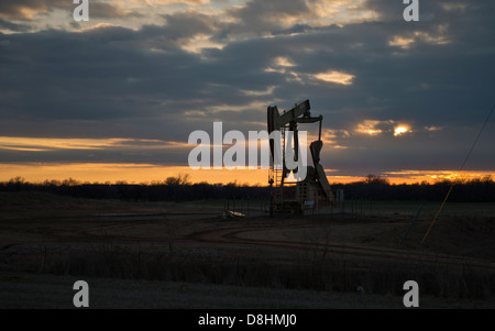 A pump jack pumps oil from a well silhouetted against a sunset in Kansas, USA, United States. Stock Photo