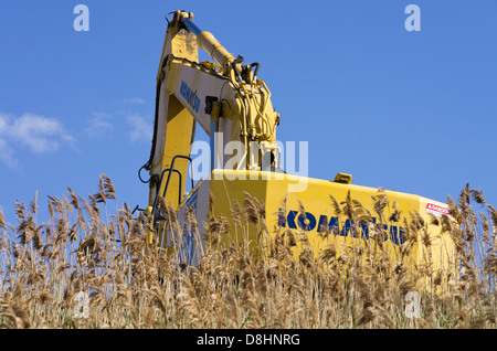 Yellow excavator digging on a grassy hill against blue sky Stock Photo