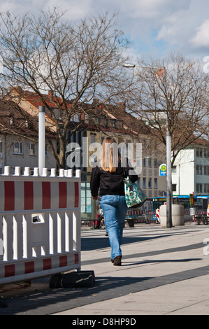 Caucasian young woman with long brown hair wearing blue jeans, walking towards a bus stop in the city - Heilbronn, Germany Stock Photo