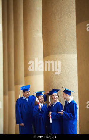 Group of smart students in graduation gowns having chat Stock Photo