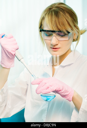 portrait of young woman scientist in lab injecting liquid with pipette into retort Stock Photo