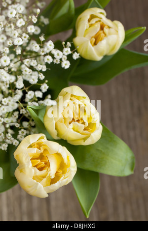 Top view on bouquet of yellow tulips and little white flowers on old wooden table Stock Photo
