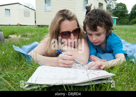 Mother and young son lying on blanket, working puzzles in newspaper together Stock Photo