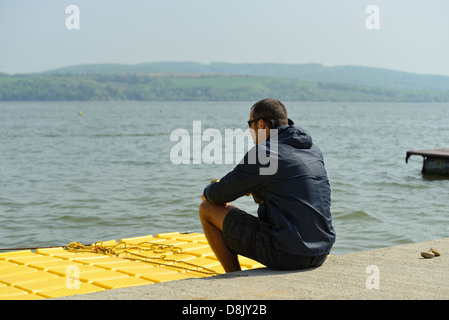 Man sitting on a floating dock looking at water Stock Photo