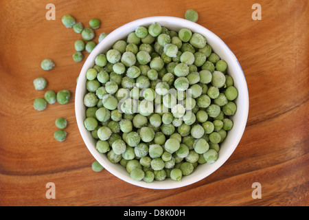 Frozen green peas in bowl on wooden surface Stock Photo