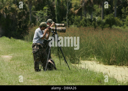 Two professional photographers are seen in the countryside, each equipped with cameras. The image captures them actively engaged in capturing the scenic landscape, highlighting the rural environment as their subject of focus. Stock Photo