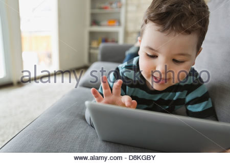 Little boy lying on sofa using digital tablet
