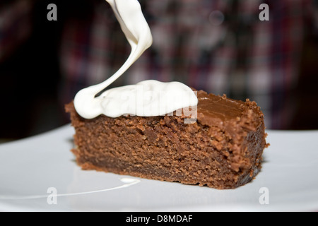 Home made moist chocolate cola cake on white plate with dollup of fresh cream on top Stock Photo