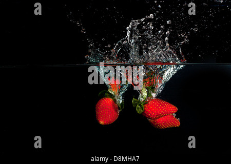 Strawberries in water with splashes on black background, horizontal Stock Photo