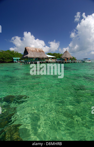 Clear waters, thatched roof bungalows and tourists at jetty in Coral Cay restaurant. Bastimentos National Marine Park Stock Photo