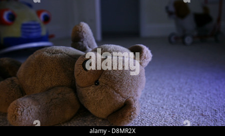 A brown teddy bear on a child's bedroom floor with other toys in the background. Open door. Stock Photo