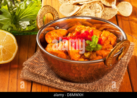 Chicken curry in a balti dish, with mini poppadums, salad and lemon. Stock Photo