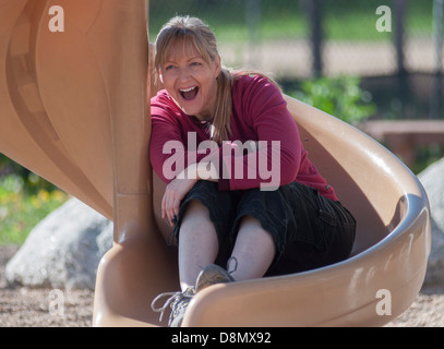 Woman sitting on a playground slide laughing. Stock Photo