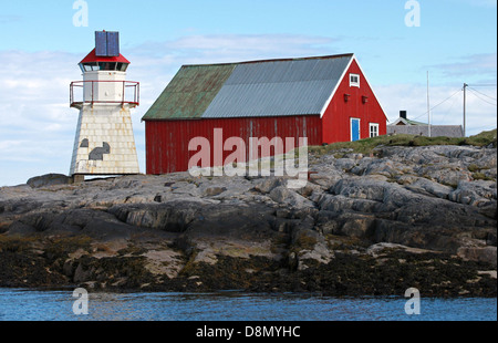 Norwegian lighthouse. White tower red top stands on coastal rocks nearby traditional red wooden house Stock Photo