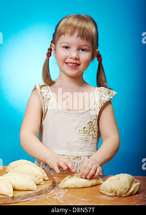 Smiling little girl kneading dough at kitchen with baking a pie Stock Photo