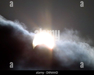 A captivating image of the sun partially obscured by clouds during an eclipse. The atmospheric conditions create dramatic lighting effects, emphasizing the unique and rare natural event. Stock Photo