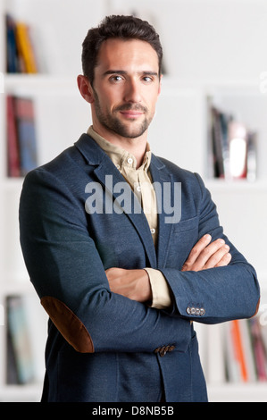 Casual business man with arms crossed with a bookshelf behind him Stock Photo