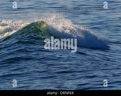 A powerful wave crashes onto the shore in the open ocean. The image captures the energy and motion of the water, highlighting the natural force of the ocean's waves. Stock Photo