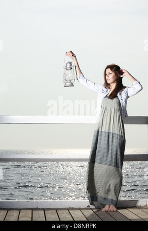 Full length young woman on pier with a oil kerosene lamp. Concept carrying light, daylight Stock Photo