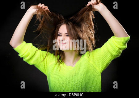 Grimacing young crazy woman making silly face pulling hair on black background Stock Photo