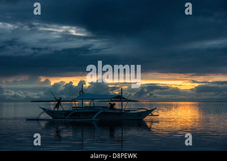 Boy pushing a bangka boat - a traditional Filipino fishing boat - with a long pole in sunset Stock Photo