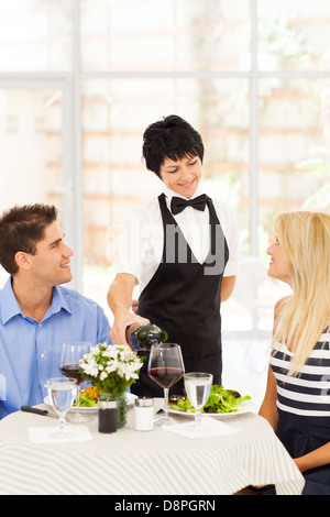 friendly mature waitress serving wine to diners in restaurant Stock Photo