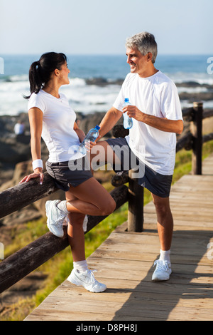 middle aged couple drinking water after exercising on beach Stock Photo