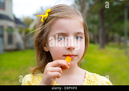 Blond kid girl eating corn snacks in outdoor park in lawn background Stock Photo