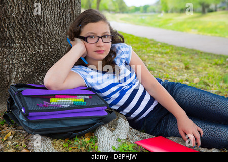 Clever student teenager girl with school bag resting relaxed under park tree Stock Photo