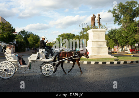 Tourists riding in a horse drawn carriage or calesa on Paseo de Montejo, Merida, Yucatan, Mexico Stock Photo