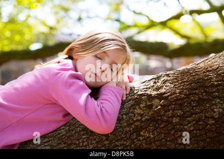 Blond children kid girl having a nap lying on a tree branch Stock Photo