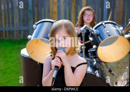 Blond kid girl singing in tha backyard with drums behind Stock Photo